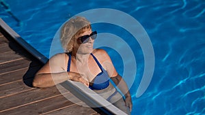 An elderly woman in sunglasses swims in the pool. Vacation in retirement.