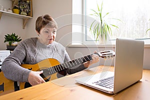 An elderly woman takes guitar lessons online. Senior retired woman studying online, watching online music lessons at