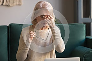 Elderly woman taking off glasses tired of computer work