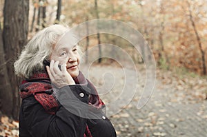 Elderly woman talking on the phone in an autumn park