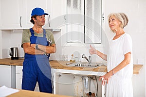 Elderly woman thanking professional plumber for work in kitchen