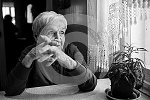 An elderly woman thinking near the window.