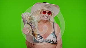 Elderly woman tourist in swimsuit bra exhales from heat or stuffiness, waves hand fan at herself