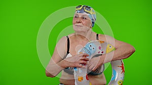 Elderly woman tourist in swimsuit bra, swim goggles with swimming ring, looking around on chroma key
