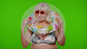 Elderly woman tourist in swimsuit dancing, celebrating, smiling with rubber ring on chroma key