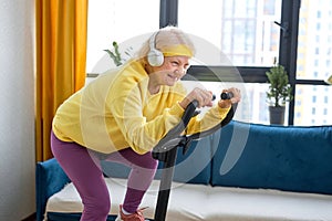 elderly woman training and doing exercise on cycle at home. active pensioner lifestyle