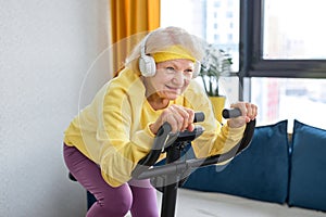 elderly woman training and doing exercise on cycle at home. sportive pensioner lifestyle