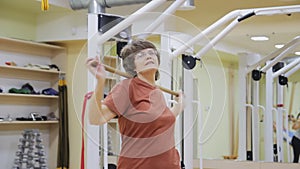 Elderly woman turning with stick, doing physiotherapy exercises in fitness room. Healthy gymnastics. Active seniors.