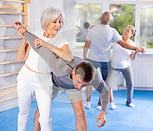 Elderly woman twists arm of attacking man with painful hold in gym. Self-defense lesson