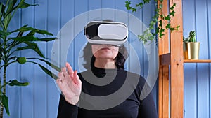 An elderly woman uses virtual reality glasses. The everyday future of the house. Older people and modern tech concept