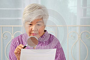 Elderly woman using a magnifying glass to reading through the lens to handheld document as her eyesight deteriorates with age