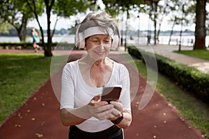 Elderly woman using mobile phone during running exercise outdoors