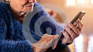 Elderly woman using mobile phone while sitting at living room home. Grandmother