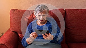 Elderly woman using a mobile phone while sitting on sofa. Grandmother smartphone