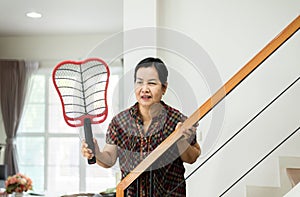 Elderly woman using mosquito swatter at home,Female with mosquito electric net racket