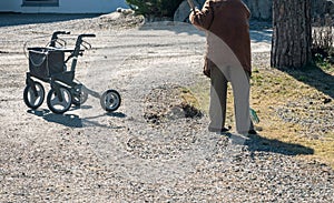 Elderly woman with walker, rakes the lawn and doing gardening work