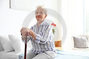 Elderly woman with walking cane sitting on bed in nursing home