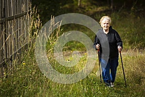 An elderly woman walks with sticks, practicing Nordic walking in the countrysideÑŽ