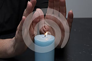 An elderly woman warms her hands with fire from a candle, selective focus. Concept: shutdowns of heating and electricity, rising