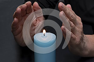 An elderly woman warms her hands with fire from a candle, selective focus. Concept: shutdowns of heating and electricity, rising