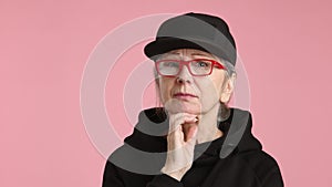 An elderly woman wearing a black hat and glasses is thinking
