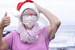 Elderly woman wearing a protective mask due to the covid-19 coronavirus standing on the beach with the ocean behind her. On his