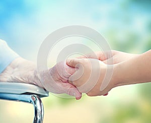 Elderly woman in wheel chair holding hands with young caretaker