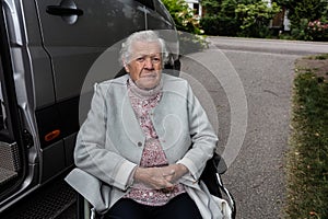 An elderly woman in a wheelchair for the disabled by a car for people with disabilities. the concept of transporting