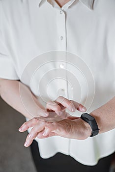 An elderly woman in a white blouse is wearing a fitness bracelet. Smart watch on the hand of an old woman. Pensioner