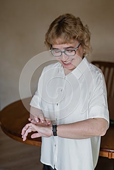 An elderly woman in a white blouse is wearing a fitness bracelet. Smart watch on the hand of an old woman. Pensioner