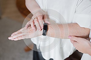 An elderly woman in a white blouse is wearing a fitness bracelet. Smart watch on the hand of an old woman. Pensioner Using Fitness