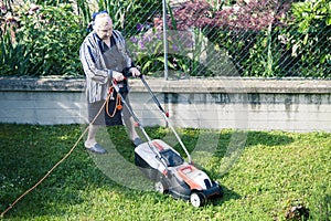 Elderly woman who cuts the grass in the garden