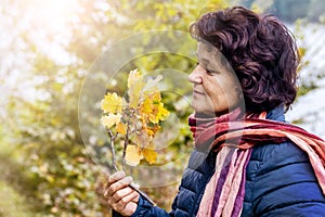 An elderly woman in the woods with pleasure examines a branch with oak leaves. Admiration of nature