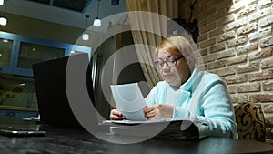 Elderly woman working at home with the documents using laptop.