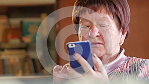 An elderly woman writes a text message on her mobile phone. She carefully presses on the screen and pronounces the text.