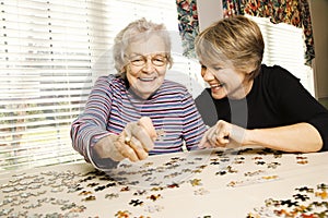 Mujer de avanzada edad y una mujer más joven a trabajar en un rompecabezas.
