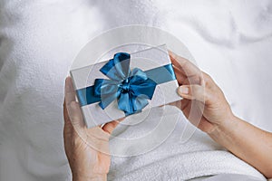 Elderly women hands holding gift box with blue ribbon and Sleep on the bed with a white blanket