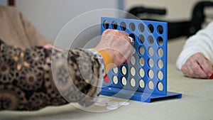 Elderly women playing a traditional strategy game to form 4 chips row at nursing home.