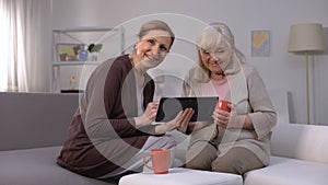 Elderly women smiling, watching entertainment show on tablet, fast internet