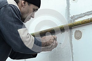 An elderly worker creates holes in the expanded polystyrene wall for the subsequent drilling and installation of an umbrella dowel