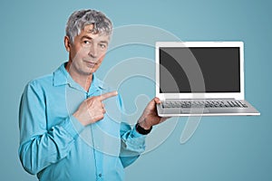 Elderly wrinked handsome male in formal shirt holds modern portable laptop computer with blank copy screen for your text or advert