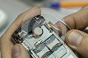 Elderly and young men repair a mobile phone together. They work in a repair shop. They use different tools.