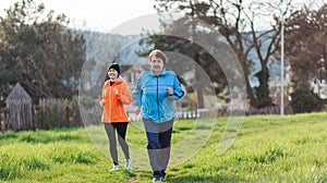 Elderly and young smiling women in sports clothes, running in the park. Grandmother and granddaughter run together