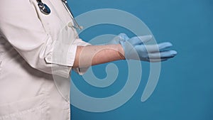 Eldery caucasian doctor lady in white coat on blue background. Close up of hands, putting gloves on