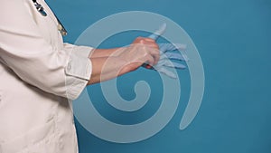 Eldery caucasian doctor lady in white coat on blue background. Close up of hands, putting gloves on