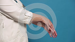 Eldery caucasian doctor lady in white coat on blue background. Close up of sanitizing hands