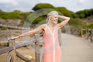 Eldery female walking along a wooden path near the beach., wearing a nice orange dress.