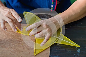 Eldery woman making and build star-shaped kite or thai name Chula kite for sale at local market.