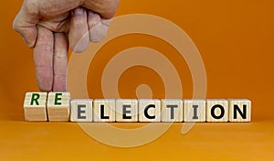 Election or reelection symbol. Wooden cubes with words `Election reelection`. Businessman hand. Beautiful orange background.