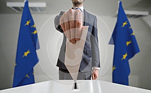 Election or referendum in European Union. Voter holds envelope in hand above ballot. EU flags in background